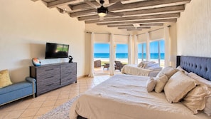 A bedroom with a bed, a TV, a sofa, and a view of the beach.