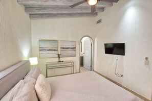 Une chambre à coucher comprenant un lit, un ventilateur de plafond, deux tableaux accrochés au mur, un téléviseur et une porte donnant sur une autre pièce.