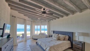 Een slaapkamer met een bed, een televisie, een plafondventilator en uitzicht op het strand.