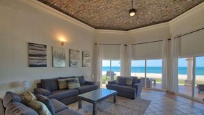 Een ruime woonkamer met een groot raam met uitzicht op het strand, een plafond met een bakstenen patroon en een moderne zithoek.