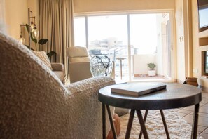 Un salon avec un canapé, une table ronde sur laquelle repose un livre, une plante en pot et une vue sur l’extérieur.