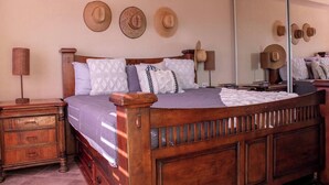 A wooden bed with a headboard, a nightstand, a lamp, and three hats on the wall.
