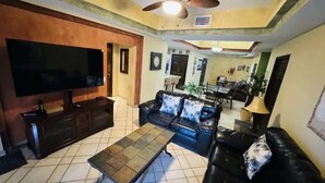 Una sala de estar con televisor, sofá, mesa de centro y un comedor con sillas y una mesa.