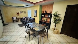 Un espace repas comprenant une table et des chaises, un canapé, une petite table ronde avec un fauteuil et une plante en pot.