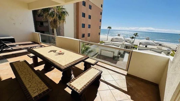 Un balcon avec une table et des bancs, donnant sur une plage et un immeuble.