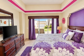 A hotel room with a bed, a TV on a dresser, a balcony with curtains, and a view of the outside.