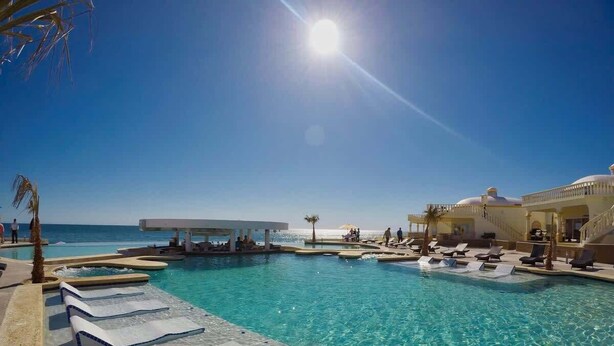 Un área de piscina con tumbonas, cielo despejado y vista al océano.