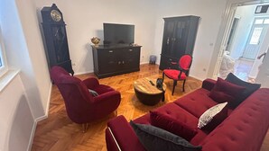 Ein Wohnzimmer mit einem roten Sofa, zwei roten Sesseln, einem Holztisch, einem Fernseher auf einem schwarzen Schrank und einem roten Sessel sowie einem schwarzen Schrank.