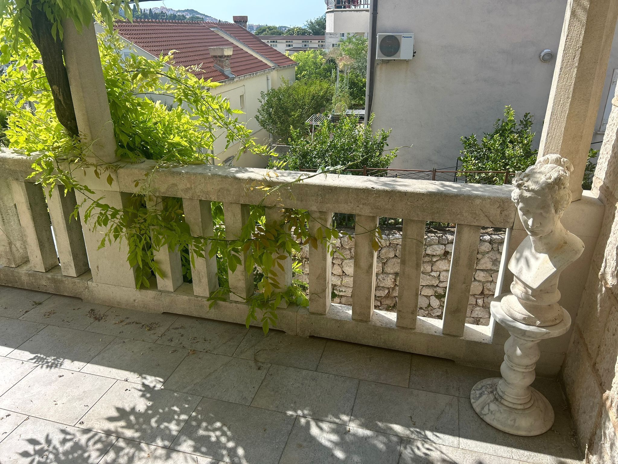 Een balkon met een stenen balustrade, een standbeeld en uitzicht op gebouwen en bomen.