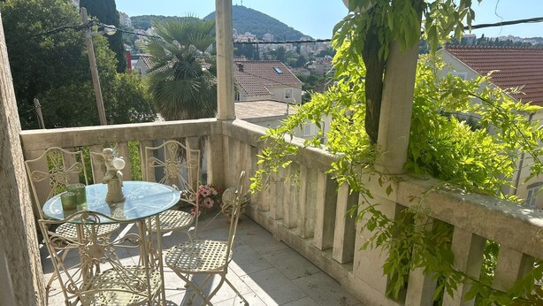 Ein Balkon mit Glastisch und Stühlen, einer Statue und Blick auf Gebäude und Hügel.
