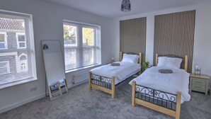 Ein Schlafzimmer mit zwei Einzelbetten, einem Heizkörper, einem Fenster mit Jalousien und einer Deckenleuchte.