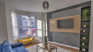 Ein modernes Wohnzimmer mit einem blauen Sofa, einem Couchtisch, einem an der Wand montierten Fernseher, einer gelben Bank und einem Topf mit Pflanze.