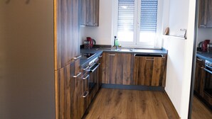 A kitchen with wooden cabinets, a built-in oven, and a window with blinds. - Apartment New York (Forheim)