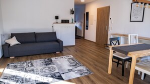 A modern living room with a grey sofa, a wooden dining table, and a patterned rug. - Apartment New York (Forheim)