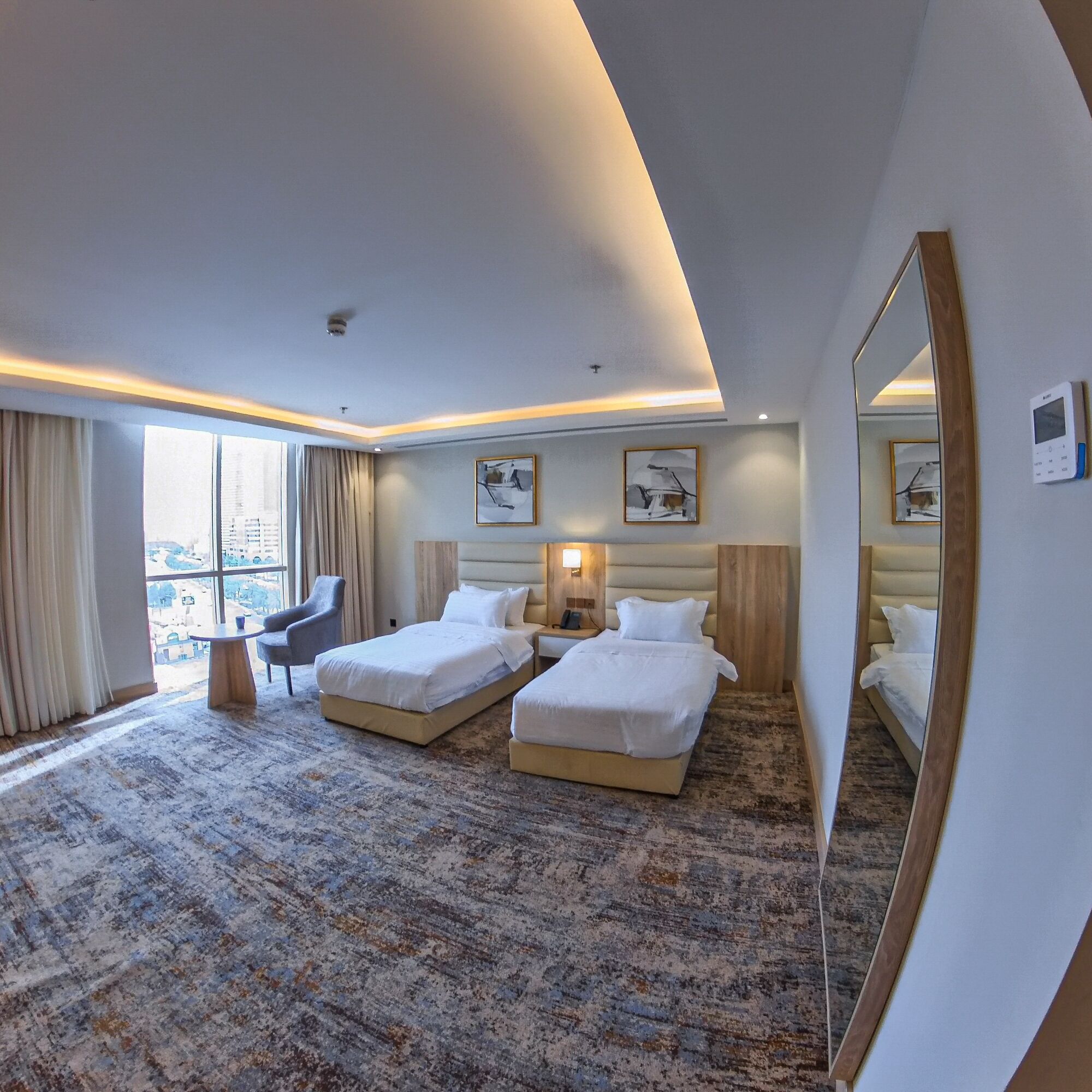 A hotel room with two beds, a desk, a chair, a large window, and a mirror.