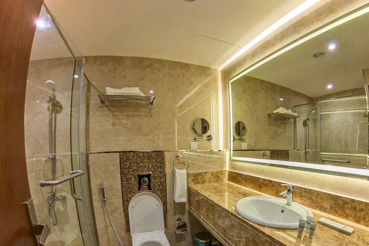 A modern bathroom with a glass shower enclosure, a toilet, a sink, and a large mirror.