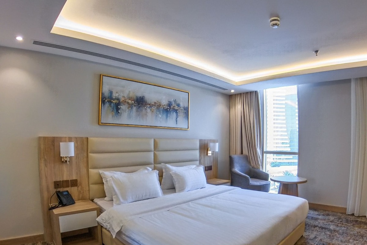 Une chambre d’hôtel moderne avec un grand lit, une table de chevet avec un téléphone, une chaise et une petite table.