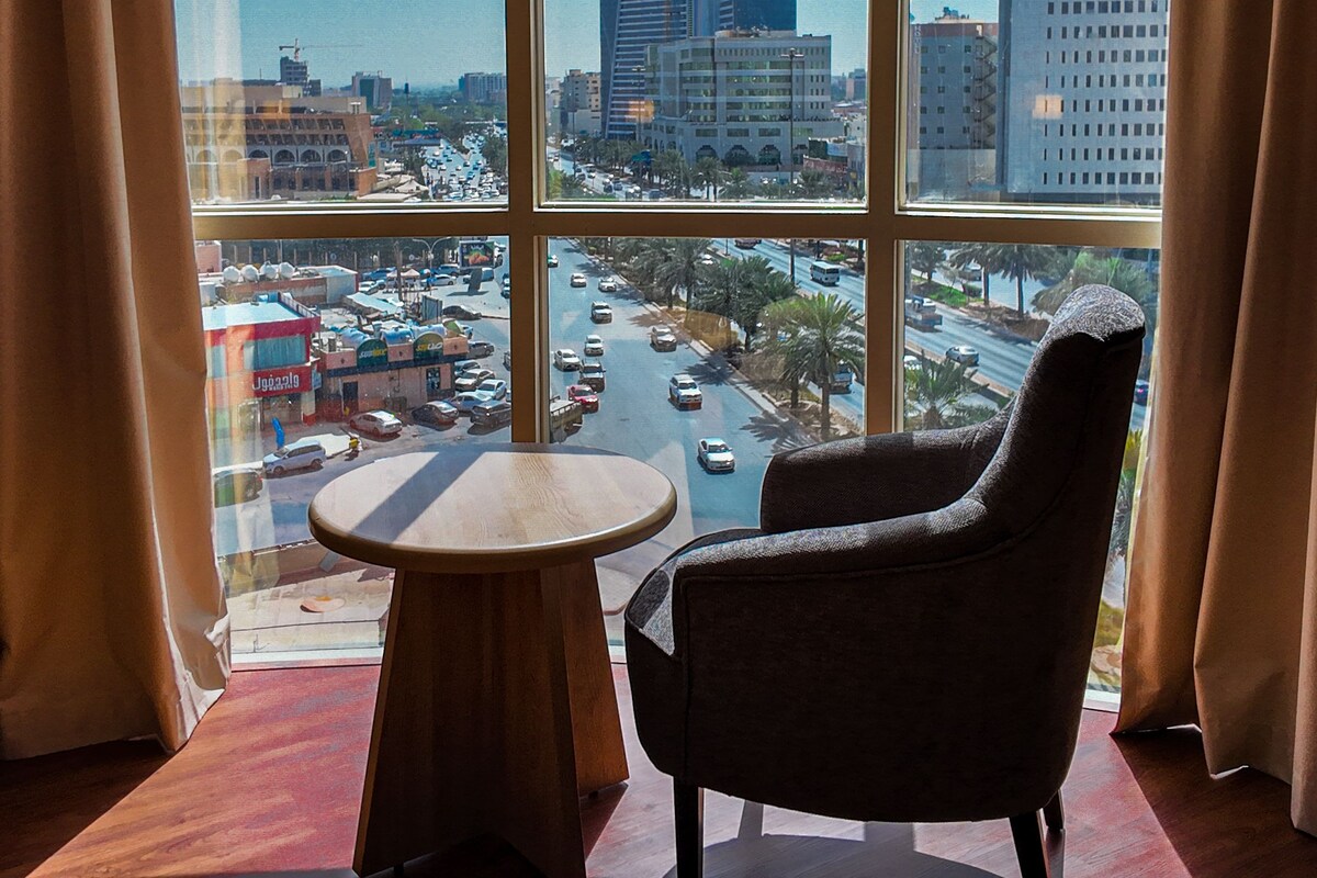 A room with a large window offering a view of a cityscape, including tall buildings and a busy street.