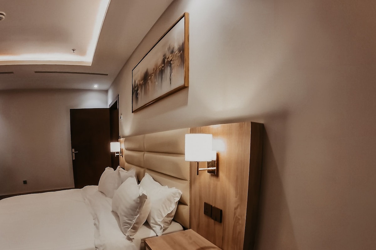 Une chambre d’hôtel avec un grand lit, une tête de lit en bois, des lampes de chevet et un tableau au mur.