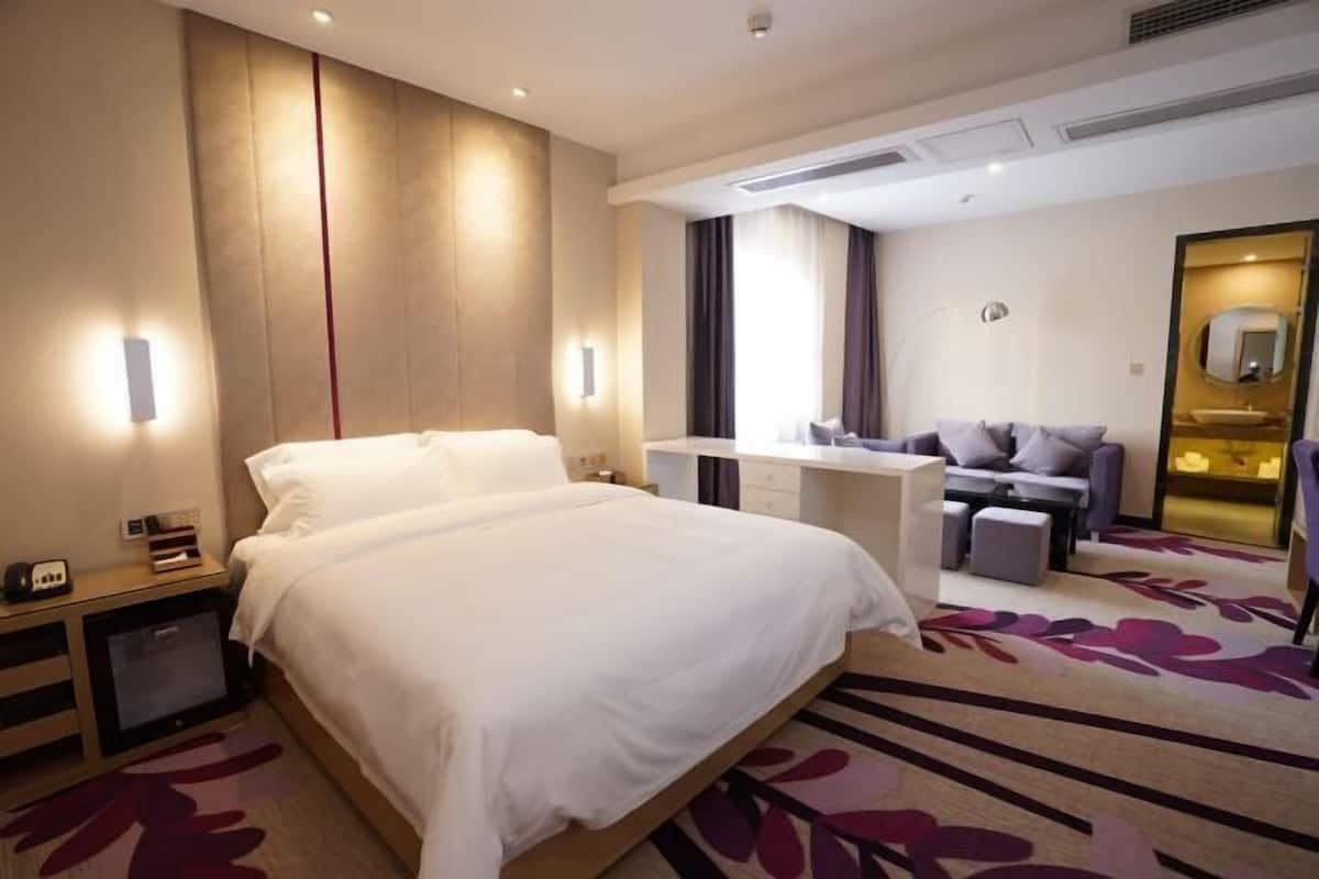 A hotel room with a large bed, a desk, a sofa, and a mirror.