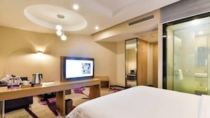 A hotel room with a bed, a desk with a television, a mirror, and a bathroom visible through a glass door. - Lavande Hotel (Qingyuan City Square Feilai Lake Branch) (Qingyuan)