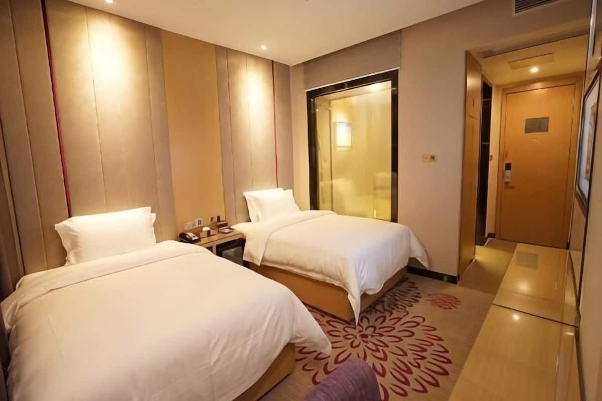 A hotel room with two beds, a nightstand, a mirror, a door, and a carpet.