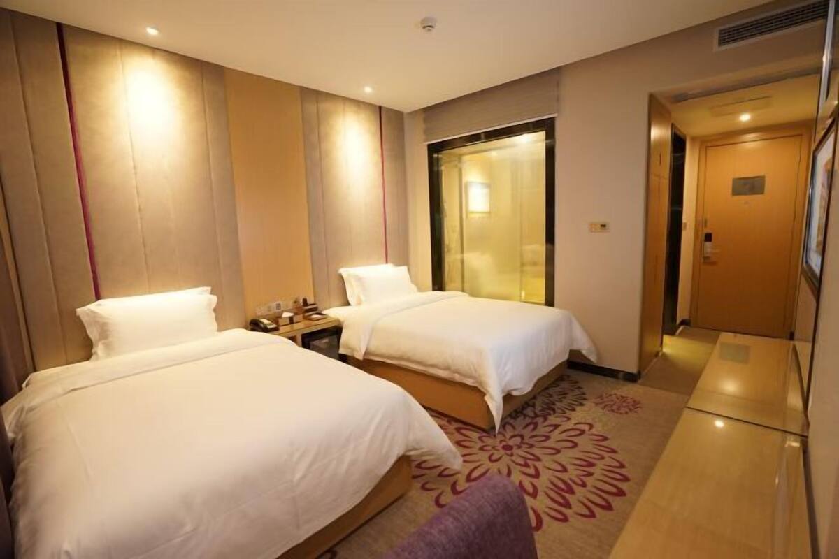 A hotel room with two beds, a nightstand, a large mirror, and a door leading to a hallway.