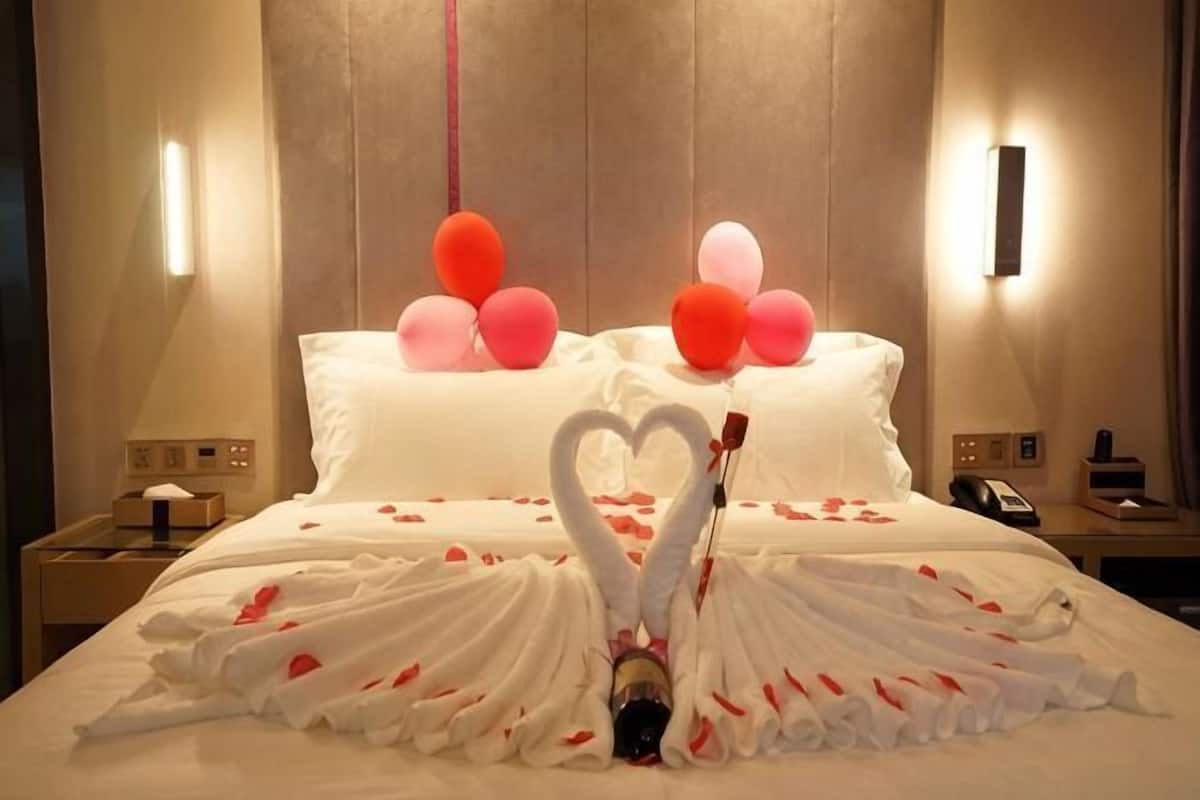 A hotel room with a bed adorned with a heart-shaped towel arrangement and balloons.