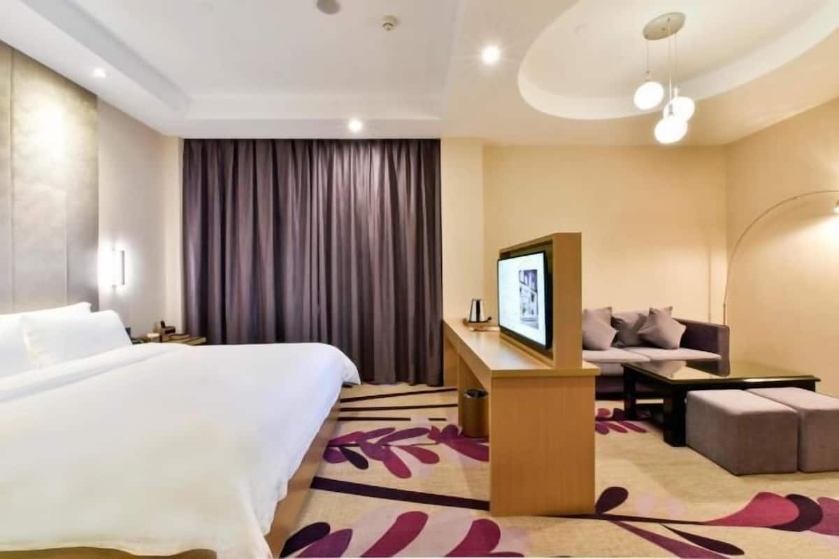 A hotel room with a bed, a desk, a sofa, and a television.