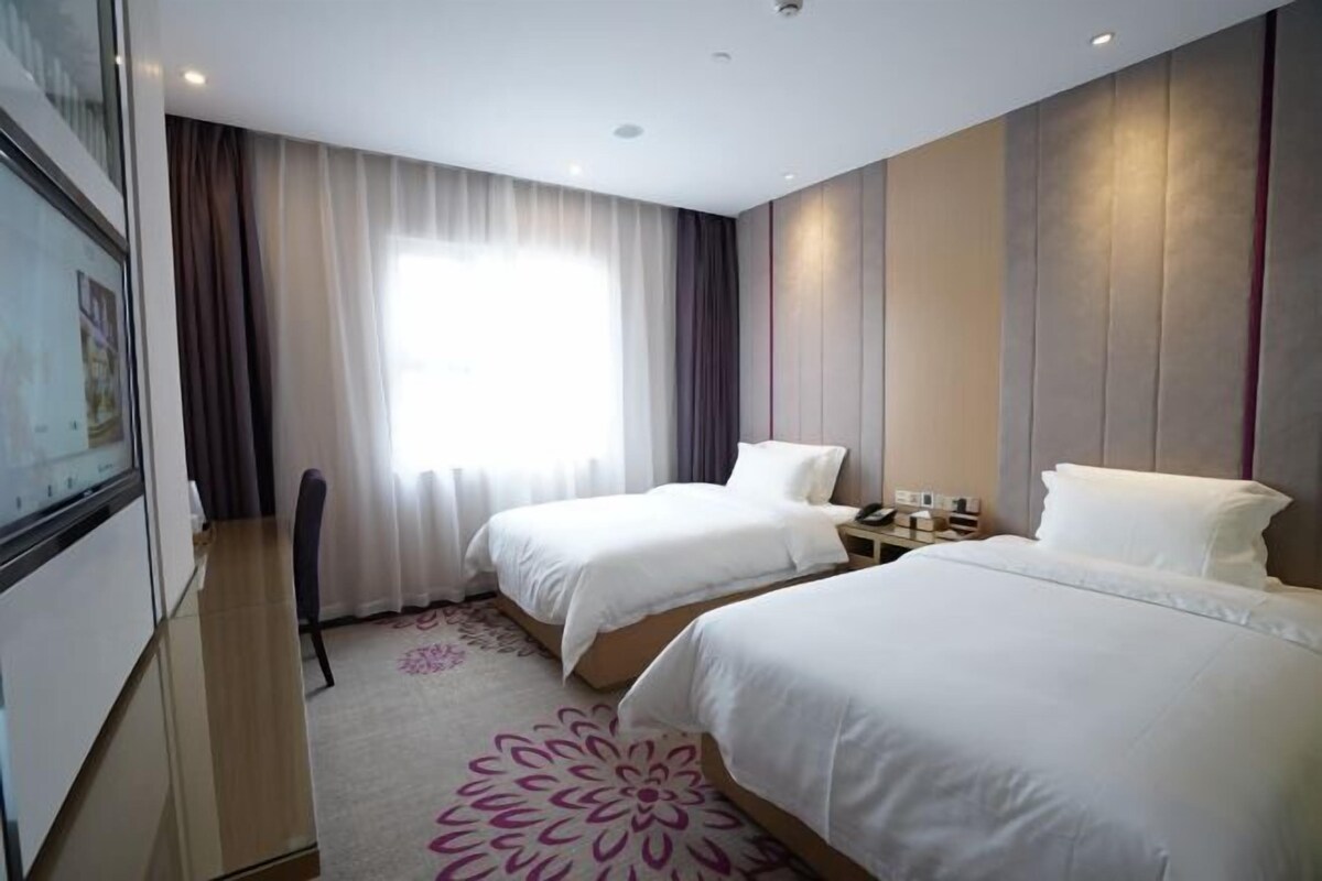 A hotel room with two beds, a desk, a chair, and a large window with curtains.