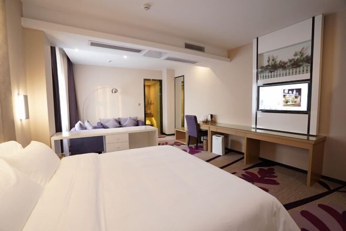 A hotel room with a large bed, a desk, a chair, a small table, a mirror, and a window with a view.