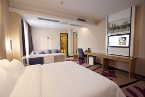 A hotel room with a large bed, a desk, a chair, a small table, a mirror, and a window with a view.
