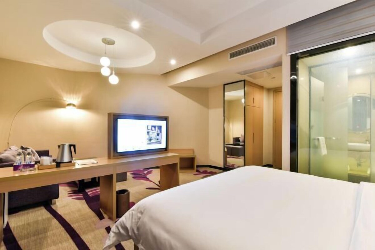 A hotel room with a bed, a desk with a television, a mirror, and a window.