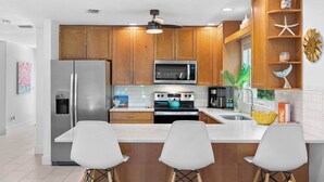 A modern kitchen with wooden cabinets, stainless steel appliances, a central island with bar stools, and decorative items on the shelves.