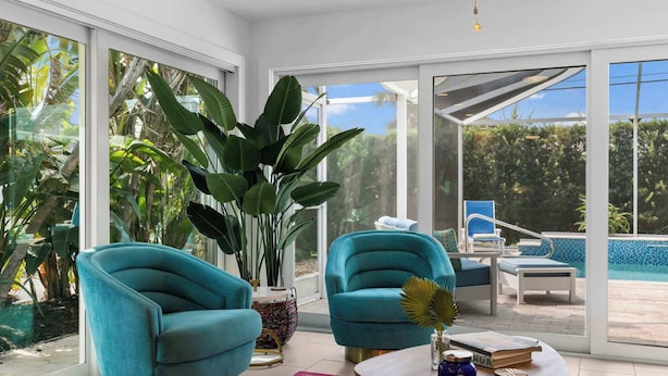 A modern living room with large windows, a pool, and two teal armchairs.