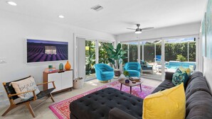 A spacious living area with a large window, a ceiling fan, and a pool visible through the glass doors.