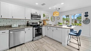 Una cocina moderna con armarios blancos, electrodomésticos de acero inoxidable, una isla grande con taburetes de bar y vistas a un jardín tropical.