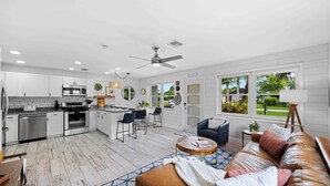 Una cocina moderna con armarios blancos, un comedor con sofá de cuero y un ventanal con vistas al exterior.