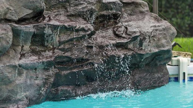 Una piscina con agua cristalina, una formación rocosa y abundante vegetación al fondo.
