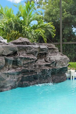 Una piscina con agua cristalina, una formación rocosa y abundante vegetación al fondo.