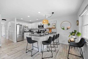 Una cocina moderna con una isla central, electrodomésticos de acero inoxidable y taburetes negros.