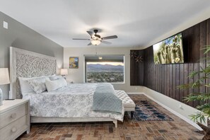 Un dormitorio con cama, ventilador de techo, mesita de noche, ventana con vistas y pared de madera.