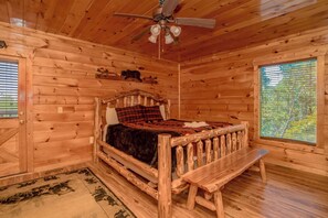 Cozy cabin bedroom with a wooden bed, bench, and ceiling fan.