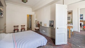 A bedroom with a large bed, a wooden door, and a dining area with a table and chairs.