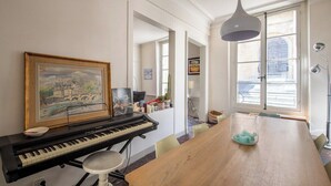 A room with a piano, a dining table, and a large window.
