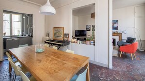 A dining area with a wooden table, chairs, a piano, and a television in the background.