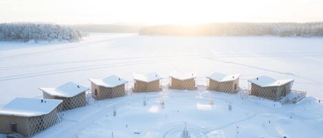A snow-covered outdoor area with several yurts arranged in a semi-circle, connected by a central pathway.