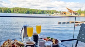 A table with breakfast items, glasses of orange juice, and a view of a lake and buildings. - Bella Lake Resort (Kuopio)