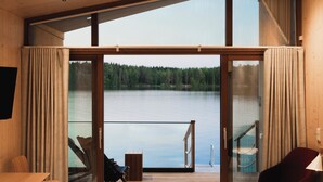 A modern room with a large sliding glass door leading to a balcony overlooking a lake. - Bella Lake Resort (Kuopio)