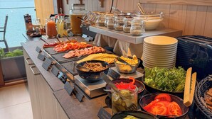 A buffet with various food items and condiments, a view of the lake, and a wooden interior. - Bella Lake Resort (Kuopio)